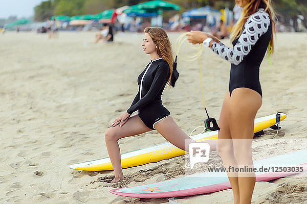 Junge Frauen dehnen sich am Strand neben Surfbrettern