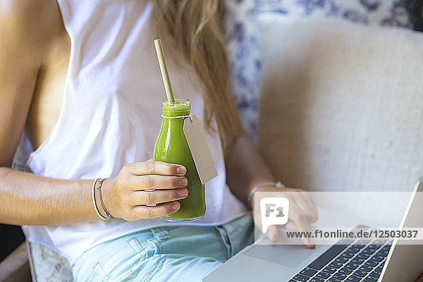 Frau benutzt einen Laptop und trinkt grünen Saft