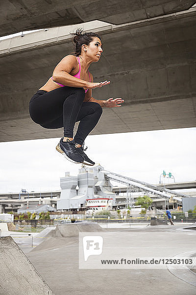 Fit Frau in Workout-Kleidung tun ein Tuck Jump in der Stadt