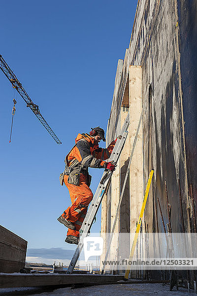 Ein Bauarbeiter klettert auf eine Leiter  um in der Höhe arbeiten zu können  während er ein traditionelles isländisches Betonhaus baut.