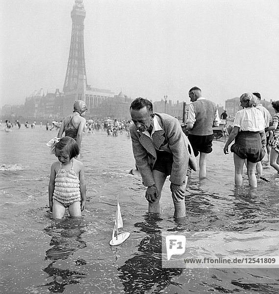 Ein Vater und seine Tochter segeln mit einer Modelljacht auf dem Meer  Blackpool  um 1946-1955. Künstler: John Gay