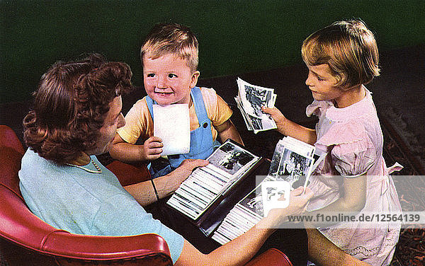 Eine Mutter und ihre Kinder sehen sich Fotos in einem Familienalbum an  Blackwood  New Jersey  USA  1956. Künstler: Unbekannt