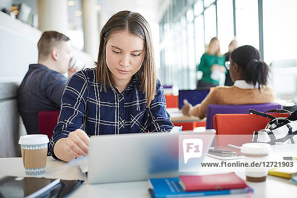 Female student using laptop at table with friends in background