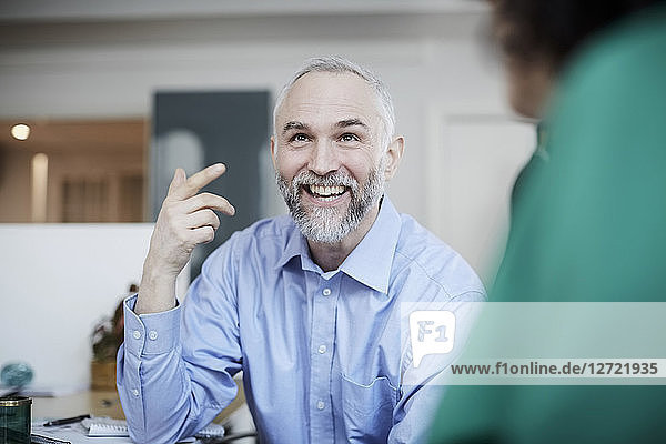 Smiling businessman gesturing while discussing female colleague at desk