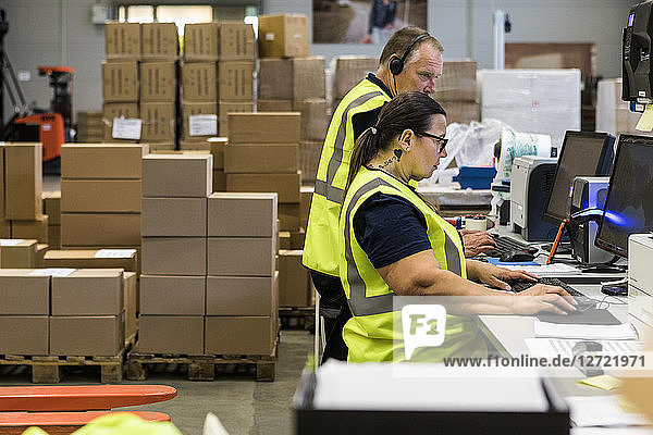 Side view of confident workers using computers at desk in distribution warehouse