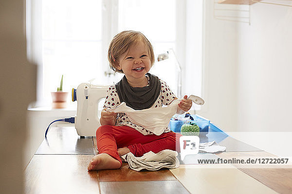 Cheerful girl wearing scarf while sitting on table against sewing machine at home