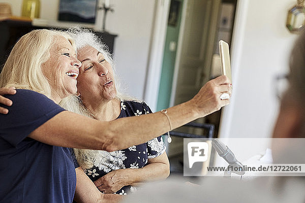Happy senior friends taking selfie on mobile phone while vlogging at home