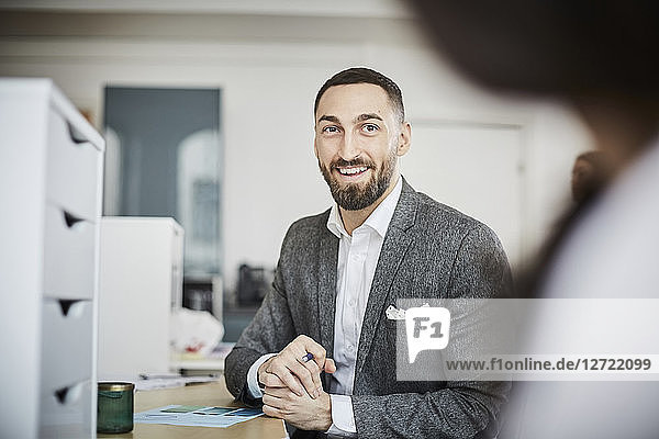 Smiling businessman looking at coworker while sitting in office
