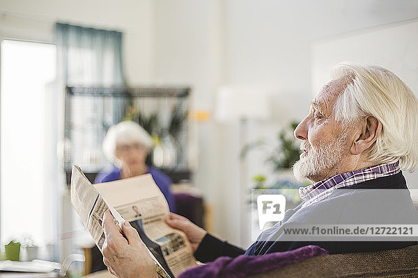 Senior man reading newspaper while sitting on sofa in nursing home