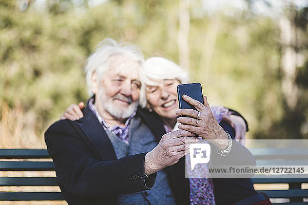 Smiling senior couple taking selfie while sitting on bench