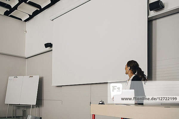 Businesswoman giving presentation while looking at blank projection screen at creative office