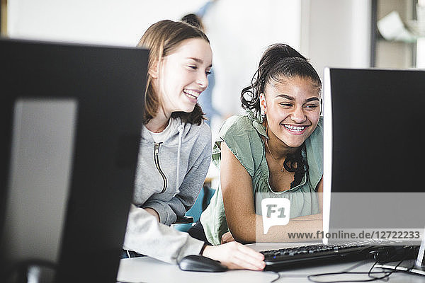 Cheerful multi-ethnic teenage girls discussing at desk in computer lab at high school