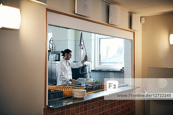 Male chef washing dishes seen through kitchen window