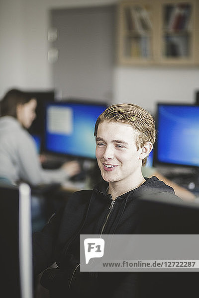 Smiling high school teenage student using computer in classroom