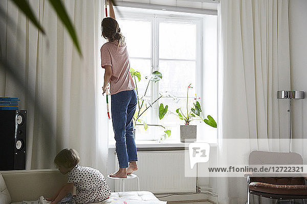 Full length of fashion designer measuring curtain while daughter playing on sofa at home