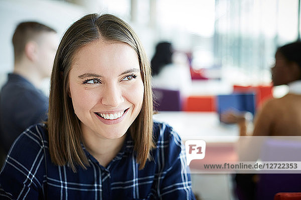 Close-up of smiling woman looking away while sitting at university cafeteria