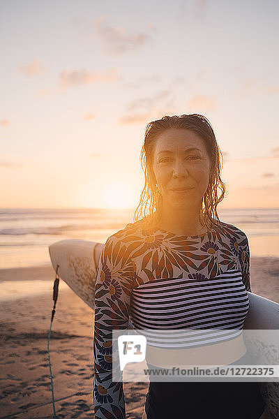Portrait of confident woman with surfboard at beach during sunset