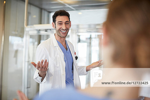 Cheerful young male doctor gesturing to female nurse while standing in lobby at hospital