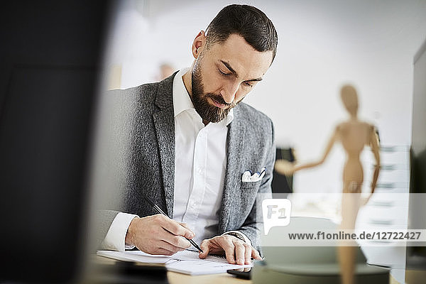 Mid adult businessman writing in note pad at desk in office