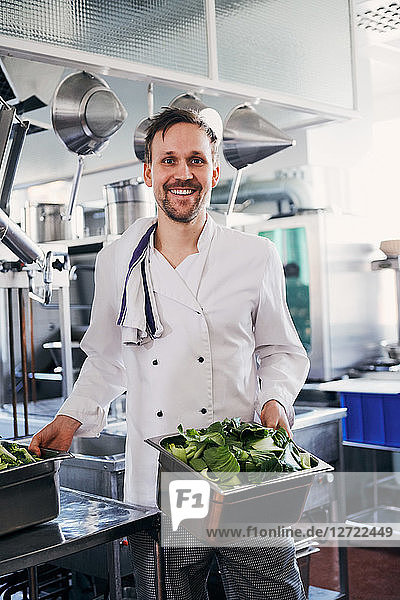 Portrait of smiling male chef holding containers of vegetables in kitchen