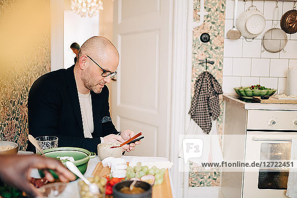 Mature man using mobile phone while sitting at dining table during party