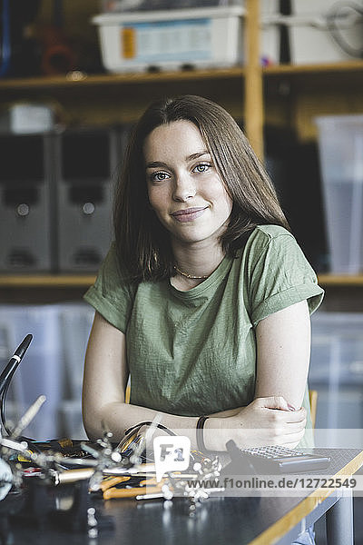 Portrait of confident female student sitting with science project at desk in classroom at high school