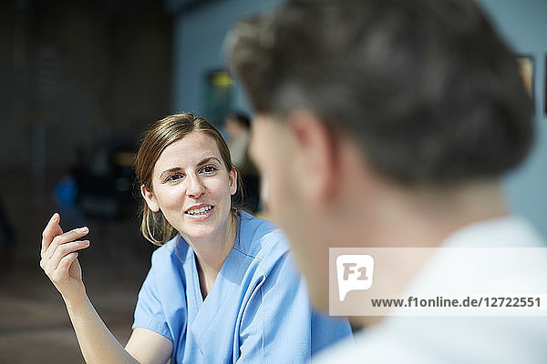 Smiling female nurse discussing with mature doctor while sitting at cafeteria in hospital