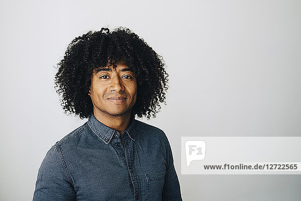 Portrait of confident businessman with curly hair standing against white wall at creative office