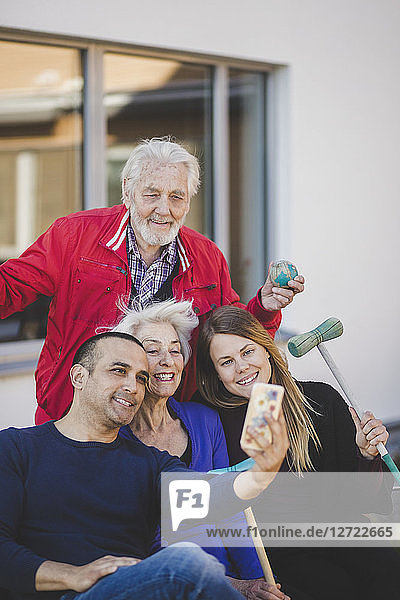 Cheerful multi-generation family taking selfie outside nursing home