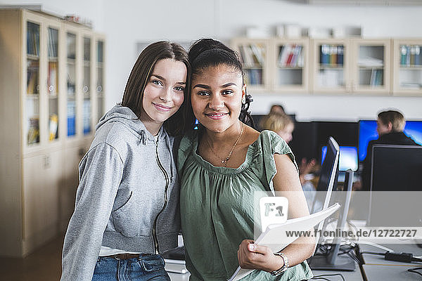 Portrait of happy female teenage friends standing in computer lab at high school
