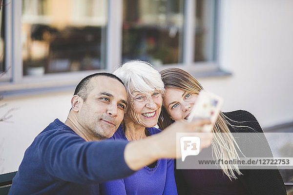 Multi-generation family smiling while taking selfie outside nursing home