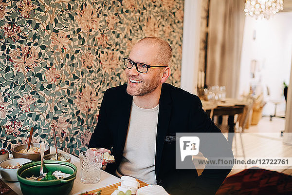 Smiling mature man looking away while sitting with food at table