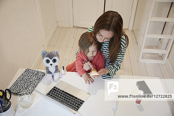 High angle view of blogger holding beauty product while sitting with daughter at table