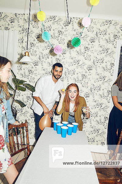 Confident young woman playing beer pong on table by male friend at dinner party