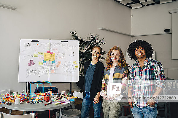 Portrait of smiling technician team standing by table and whiteboard at creative office