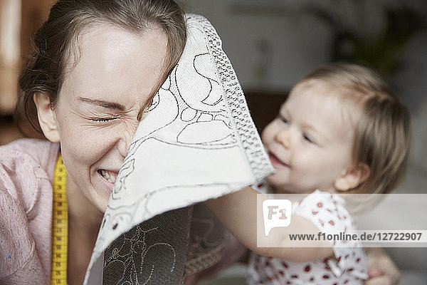 Cheerful fashion designer and daughter playing with cloth at home