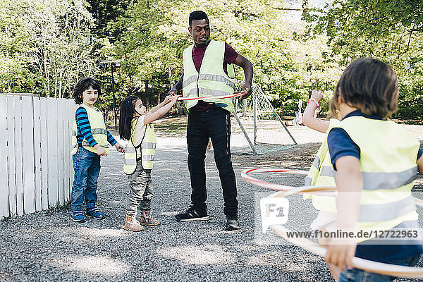 Male teacher and students playing with plastic hoops in playground
