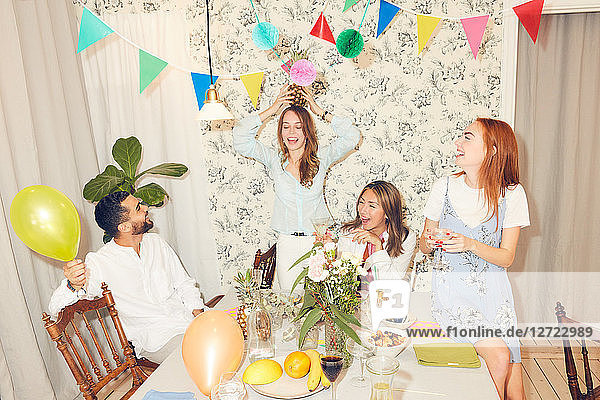 Young carefree friends playing with pineapple during dinner party at apartment