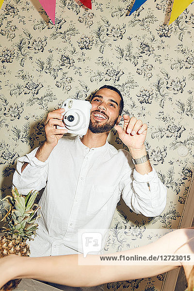 Smiling young man holding camera while sitting during dinner party at home