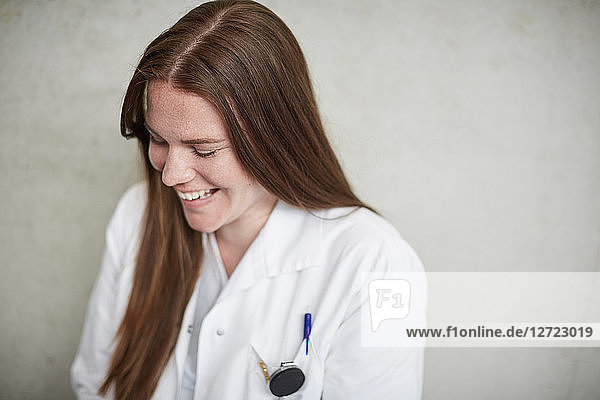 Smiling young female brunette doctor sitting against wall at hospital