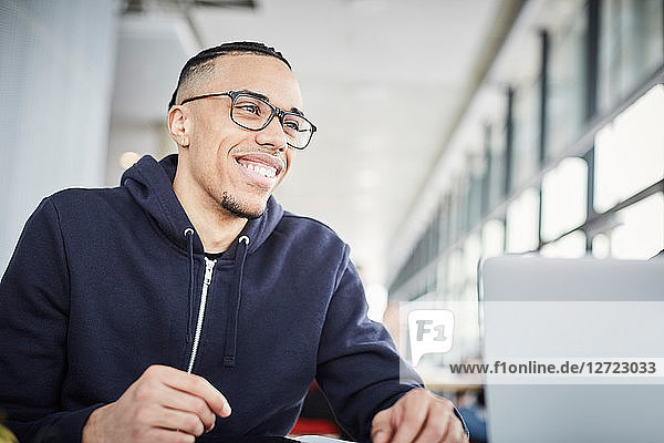 Smiling young university student looking away while sitting at table in cafeteria