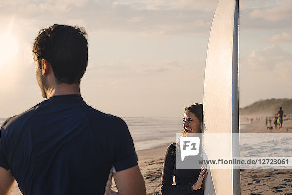 Young man with female friend holding surfboard at beach during sunset