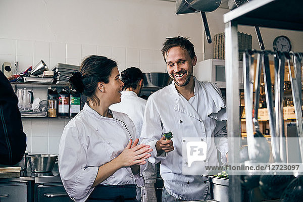 Male chef holding broccoli while talking with female colleague at kitchen