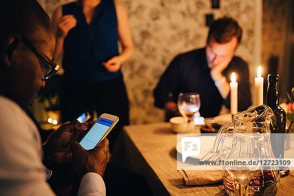 Mature man using mobile phone while having dinner with friends at party