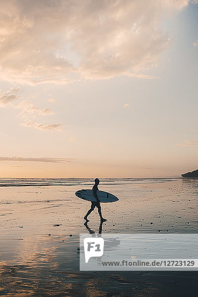 Silhouette man with surfboard walking at beach during sunset