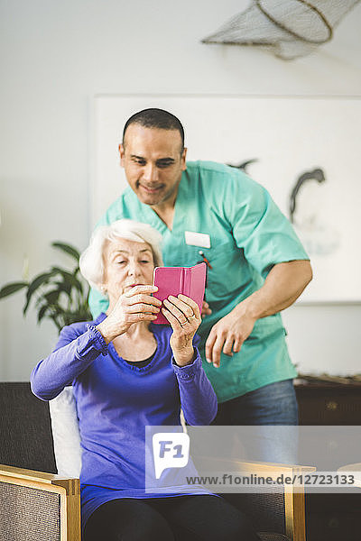 Male nurse assisting senior woman in using mobile phone at nursing home