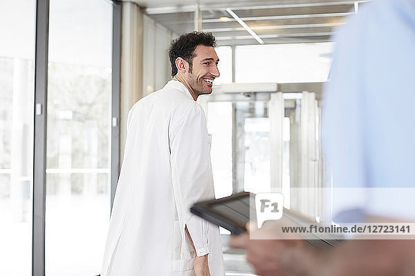 Smiling young doctor walking while male nurse holding digital tablet at lobby in hospital