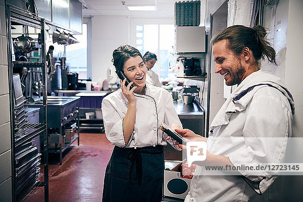 Male and female chefs using cordless phone and digital tablet in kitchen