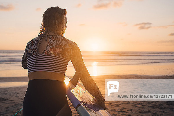 Rear view of woman with surfboard walking towards sea at beach during sunset