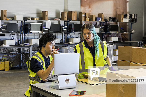 Confident young male customer service representative discussing with coworker over laptop while at desk in warehouse